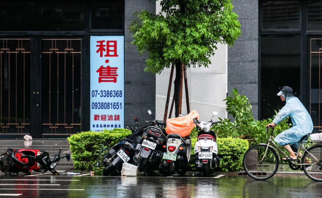 Una persona pasa en bicicleta junto a scooters que fueron derribados debido a los fuertes vientos traídos por el tifón Podul en Kaohsiung el 13 de agosto de 2025. Foto: AFP