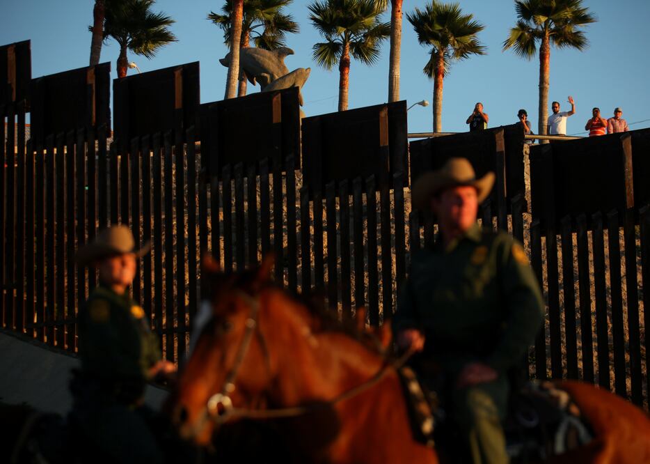 People in Mexico wave at U.S. Border Patrol agents on horseback patrolling the U.S.-Mexico border fence near San Diego, California, U.S., November 10, 2016. REUTERS/Mike Blake/File Photo