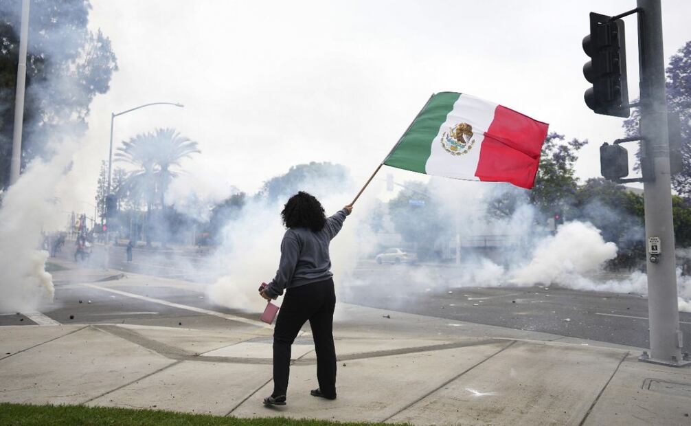 Una mujer ondea una bandera mexicana en medio de gas lacrimógeno lanzado por policías antidisturbios durante una protesta en la sección Paramount de Los Ángeles, California, el sábado 7 de junio de 2025, después de que autoridades federales de inmigración llevaran a cabo redadas migratorias. Foto: AP