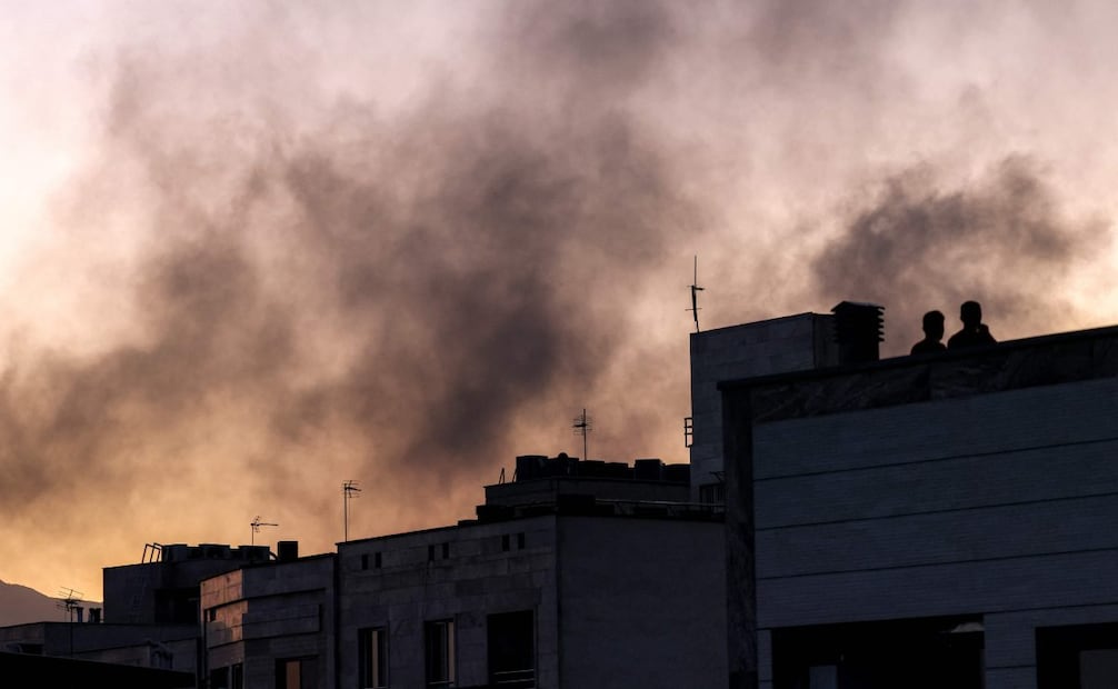 Personas en un tejado entre una columna de humo tras un ataque israelí en Teherán el 17 de junio de 2025. Foto: AFP