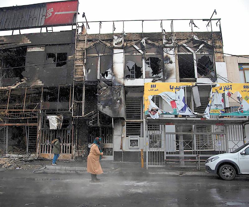 Iraníes cerca de un edificio que fue quemado durante las manifestaciones contra el gasolinazo, en Teherán. Foto: AP
