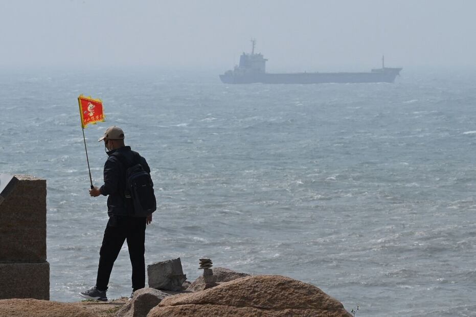 China considera a Taiwán como una provincia rebelde que debe ser recuperada. Un hombre camina con una bandera, mientras un barco pasa detrás de él en la isla de Pingtan, el punto más cercano a Taiwán, en la provincia de Fujian. Foto: AFP