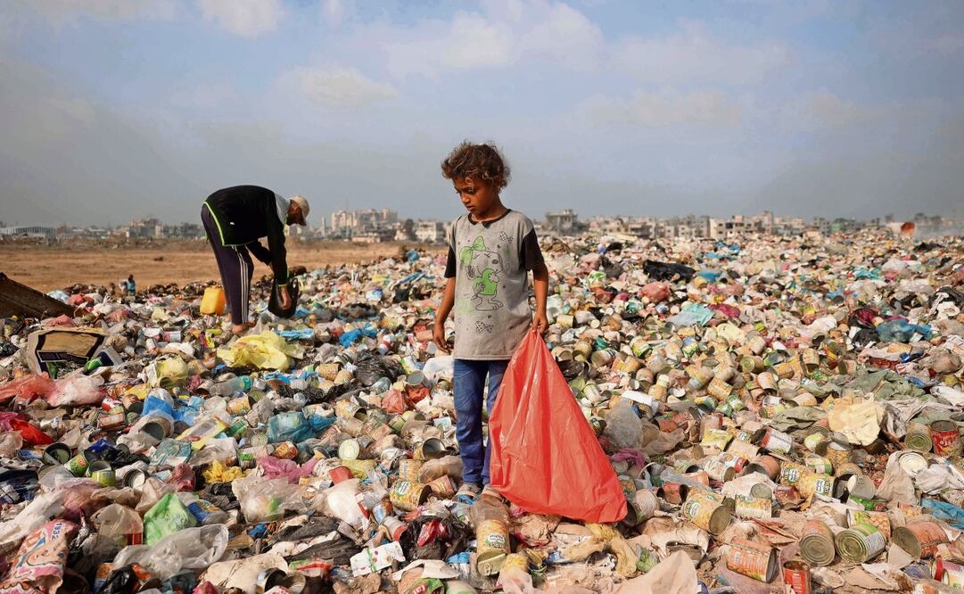 Un niño palestino desplazado busca entre la basura, en Gaza. Foto: Eyad Baba / AFP