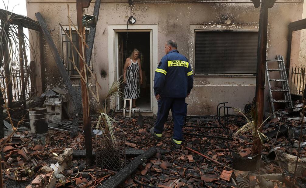 Un bombero y una mujer inspeccionan una casa quemada después de un incendio forestal en Dionysos, norte de Ática, Grecia. Foto: EFE