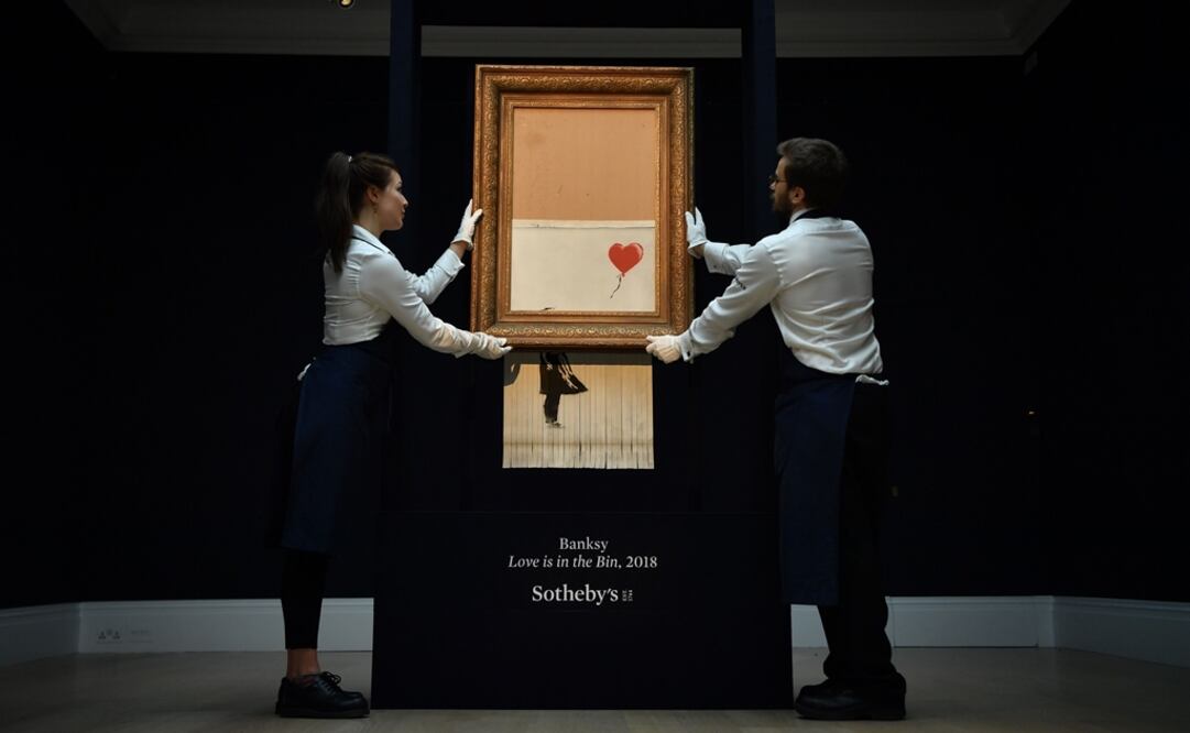 Dos empleados de Sotheby's sostienen la obra "Love is in the bin", de Banksy. Foto: Ben Stansall / AFP